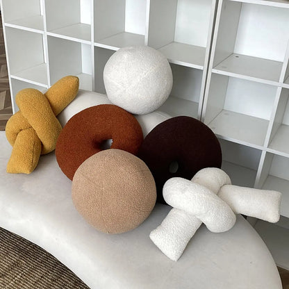 Decorative cushions in various shapes and colors on a white surface with a white shelving unit in the background.