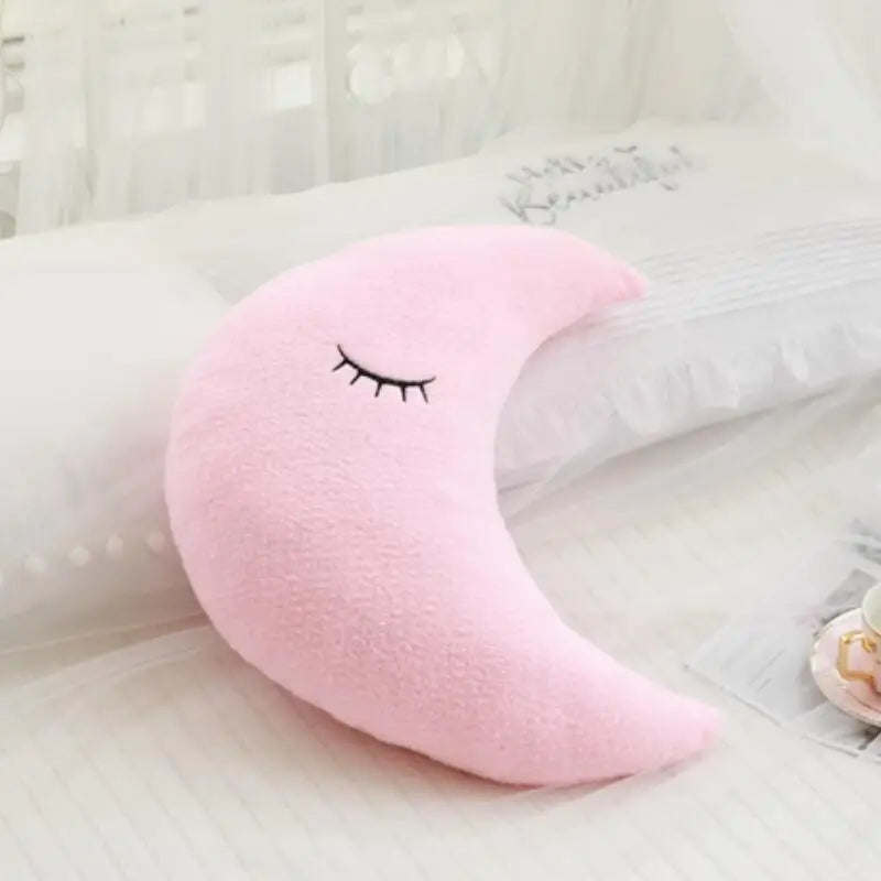 Pink crescent moon-shaped pillow with a face on a white surface