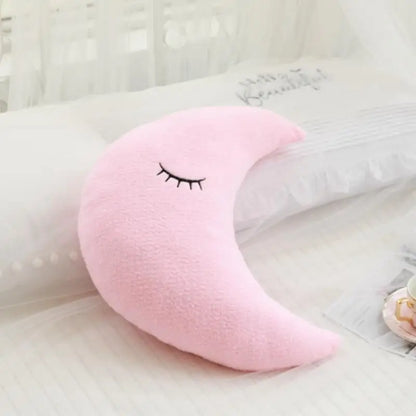 Pink crescent moon-shaped pillow with a face on a white surface