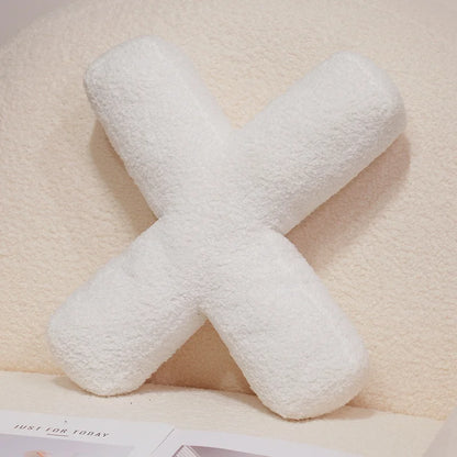 White 'X' shaped pillow on a beige surface