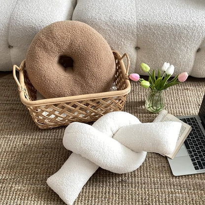 Round cushion in a woven basket on a textured surface with a laptop and flowers.
