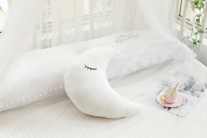 White cloud-shaped pillow on a bed with a small table and plant in the background