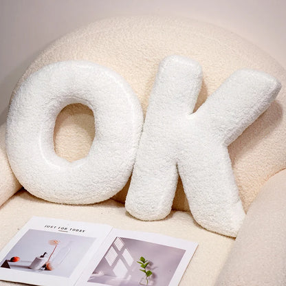 White 'OK' letter pillows on a light-colored surface with a magazine underneath.