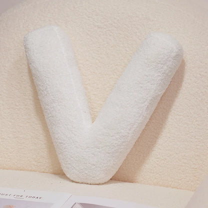 White letter 'V' pillow on a beige surface