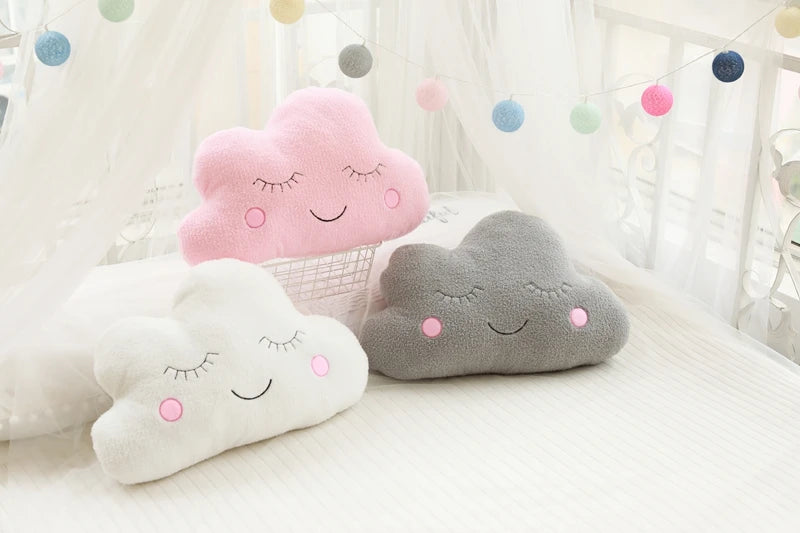 Three cloud-shaped cushions with smiling faces on a light background