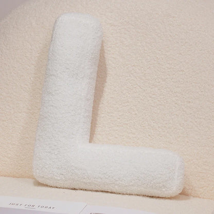 White letter 'L' pillow on a beige surface