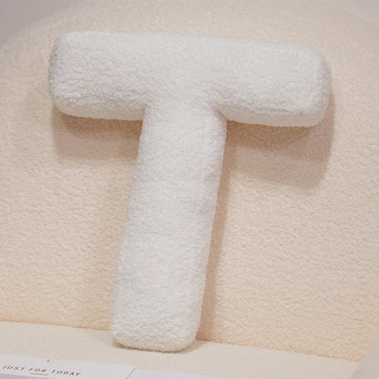 White letter 'T' pillow on a textured beige surface